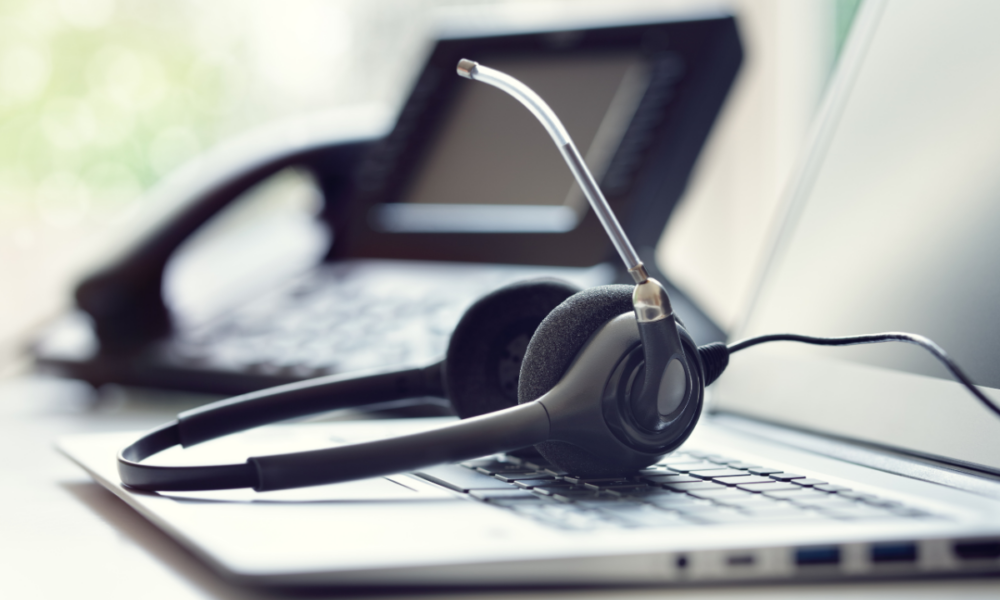 Foto di un paio di cuffie per l'assistenza IT appoggiate sopra ad un laptop davanti ad un telefono fisso.