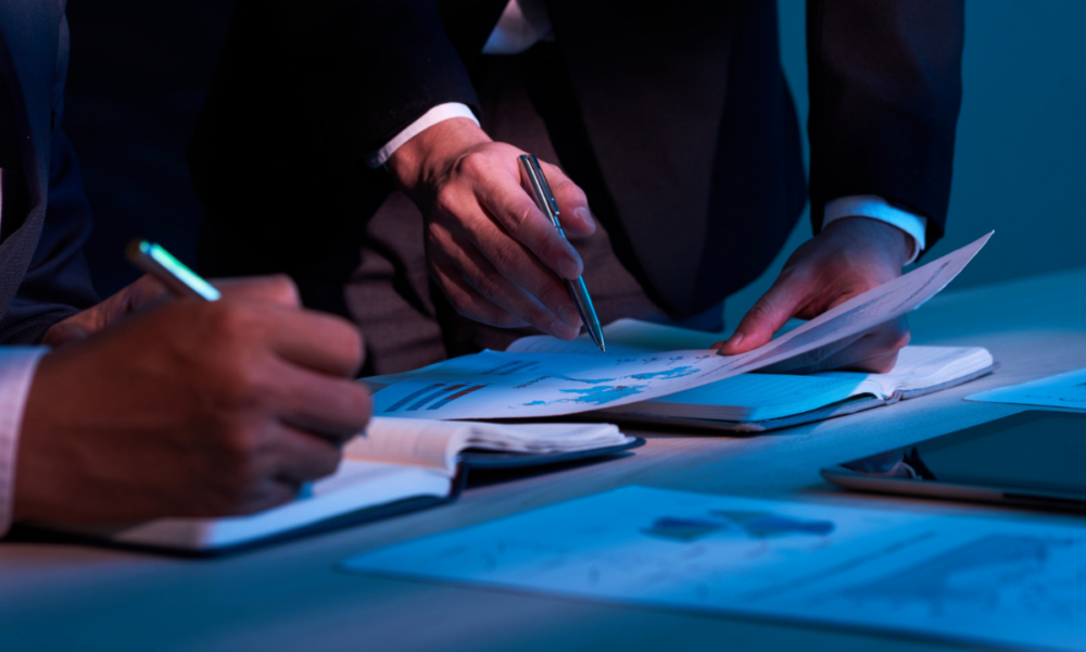 Persone in abbigliamento formale che esaminano documenti e grafici durante una riunione, simbolo di analisi funzionale e collaborazione professionale.