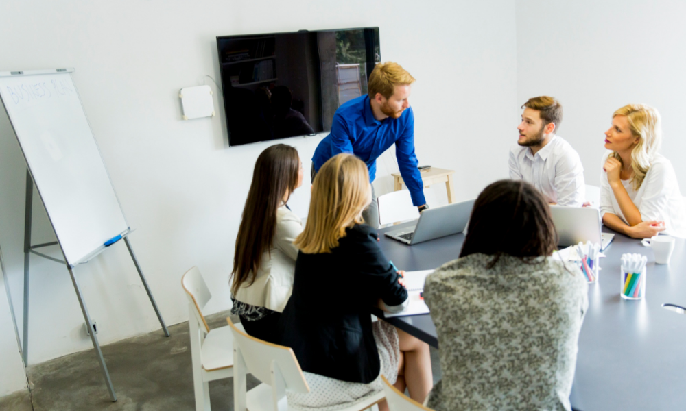 Foto di una sessione di formazione o di supporto in cui cinque persone sedute ad un tavolo stanno ascoltando un uomo in piedi.